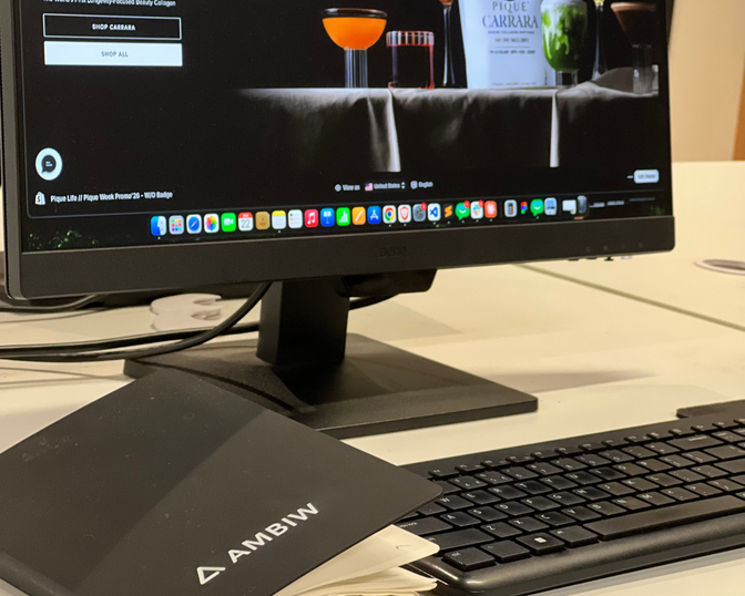 Close-up of an Ambiw agency workspace desk featuring an active e-commerce design project on a desktop monitor.