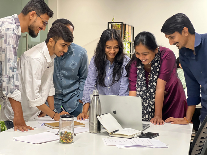 A large group of Ambiw team members smiling and celebrating a successful project launch together around a laptop.