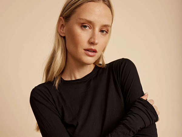 A minimalist studio portrait of a blonde woman wearing a fitted black crewneck long-sleeve top