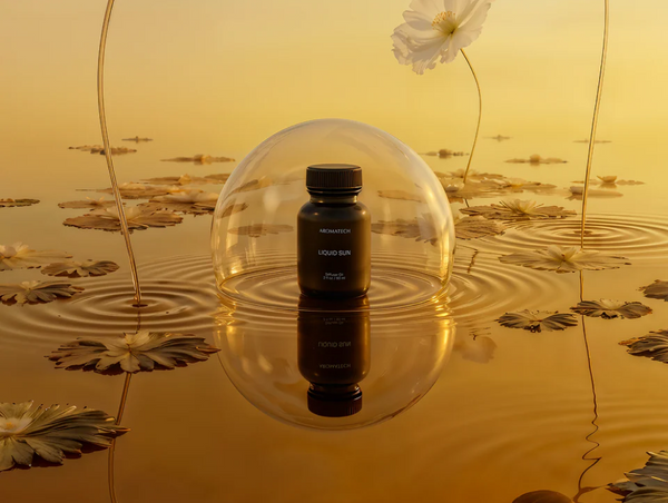 A dark bottle of Liquid Sun diffuser oil enclosed in a clear glass dome on a golden water surface filled with floating lily pads.