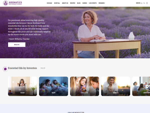Aromatics International desktop page featuring a founder's bio banner in a lavender field above an "Essential Oils by Intention" category row.