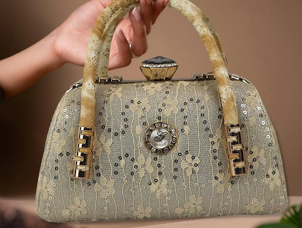 A hand holding an elegant, structured gold evening handbag covered in delicate floral lace and shimmering sequins