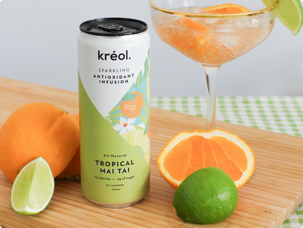 A close-up of Kréol's Tropical Mai Tai sparkling infusion can on a wooden board, surrounded by fresh oranges