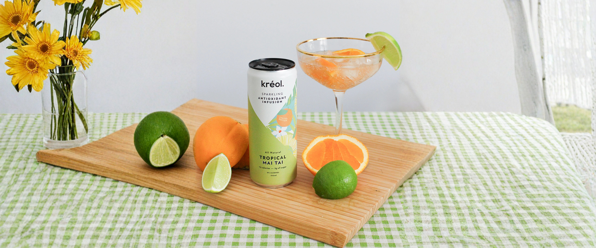 A can of Kréol Tropical Mai Tai sparkling infusion on a wooden board next to fresh oranges, limes, and a filled cocktail glass.