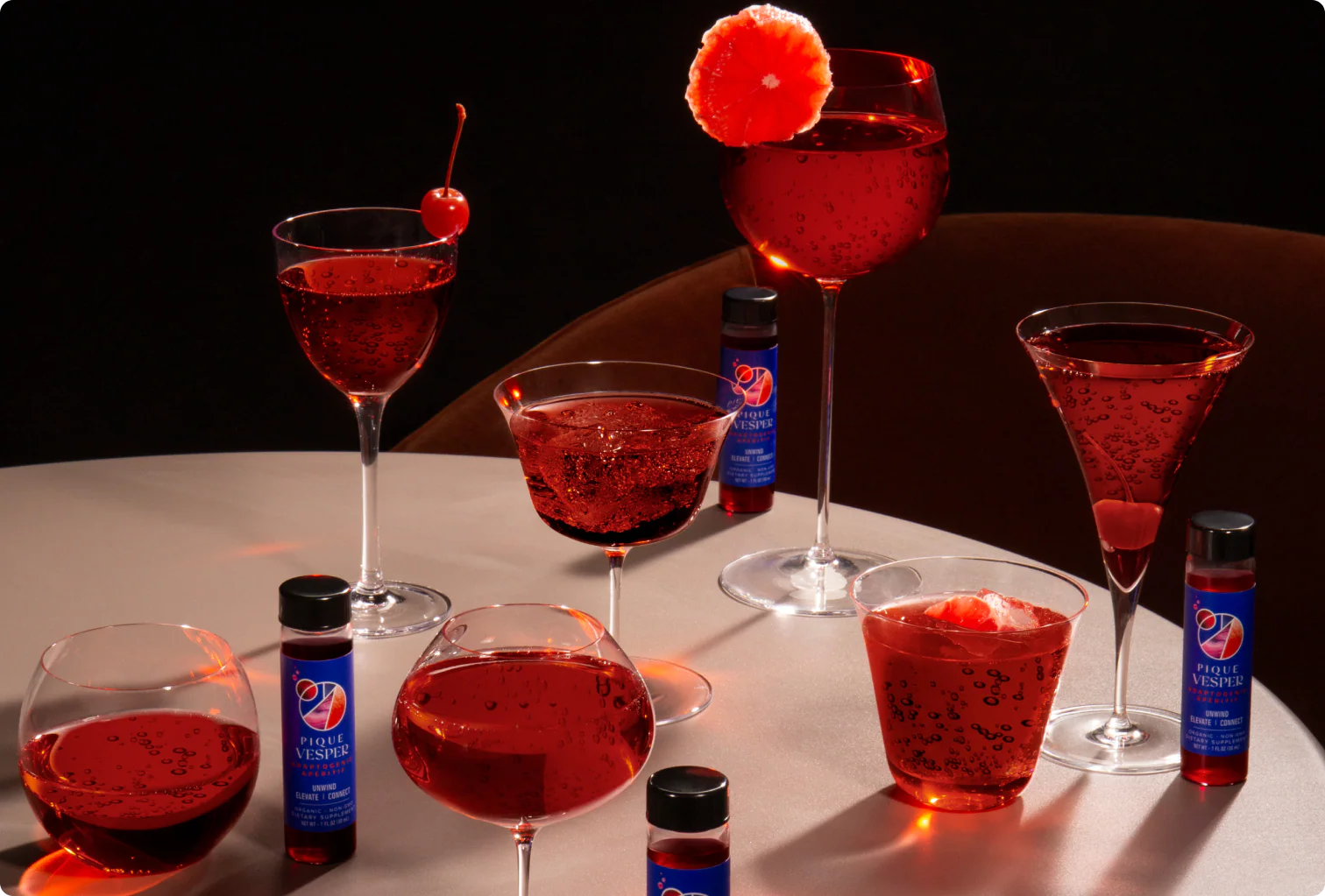 Red cocktails in various glasses with cherry and orange garnishes on a dark background.
