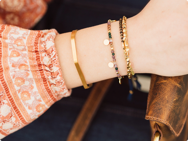 A close-up shot of a wrist wearing a curated stack of Steel & Clover bracelets